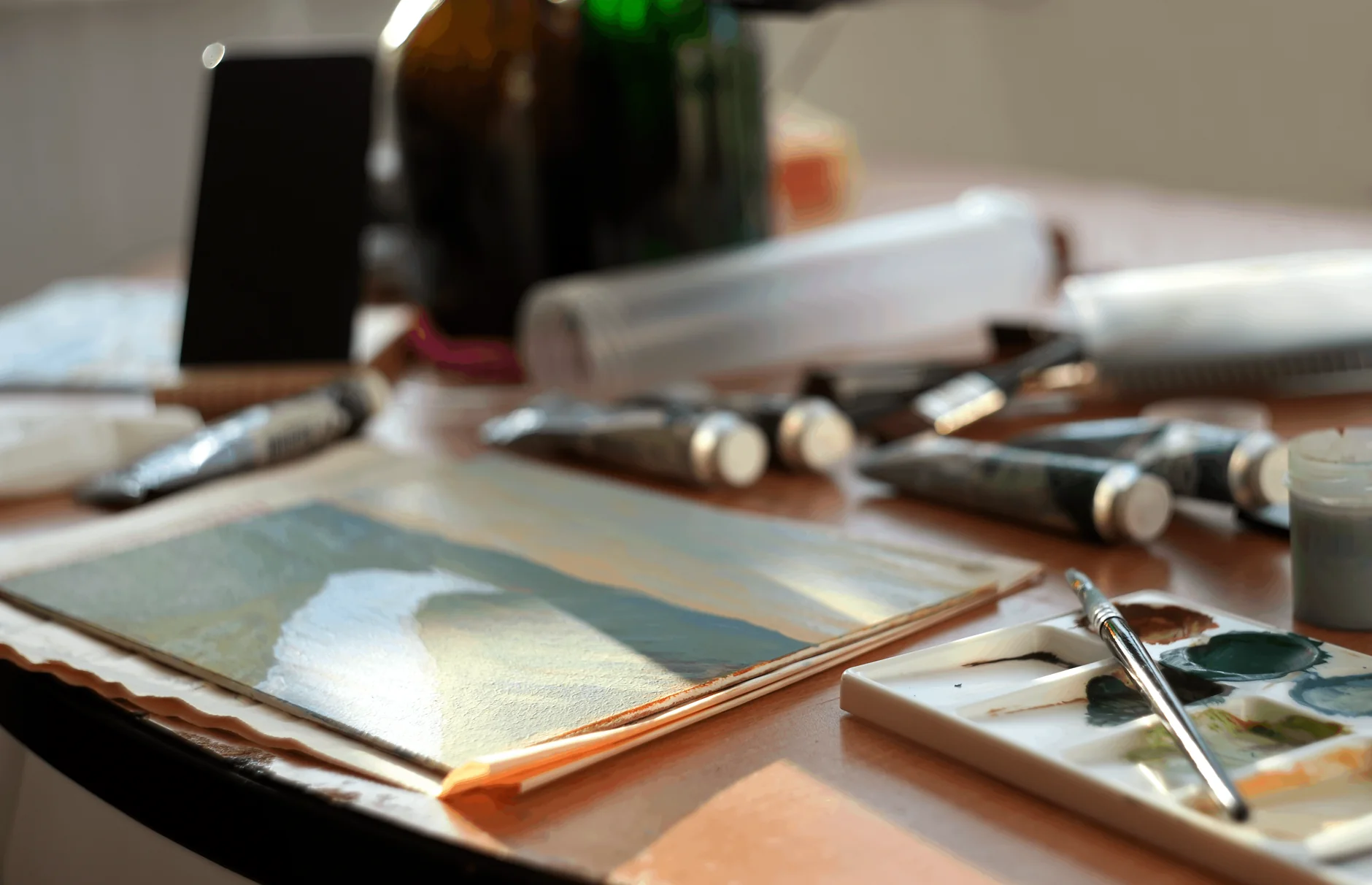 Sunlit art studio table with brushes, paint tubes, and color palette, capturing the creative process.